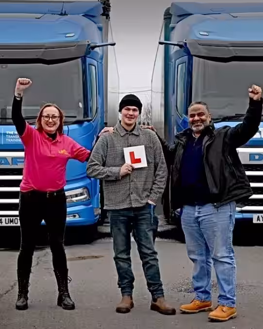 Image of Alex in front of two blue HGVs after passing HGV training course with Lifft