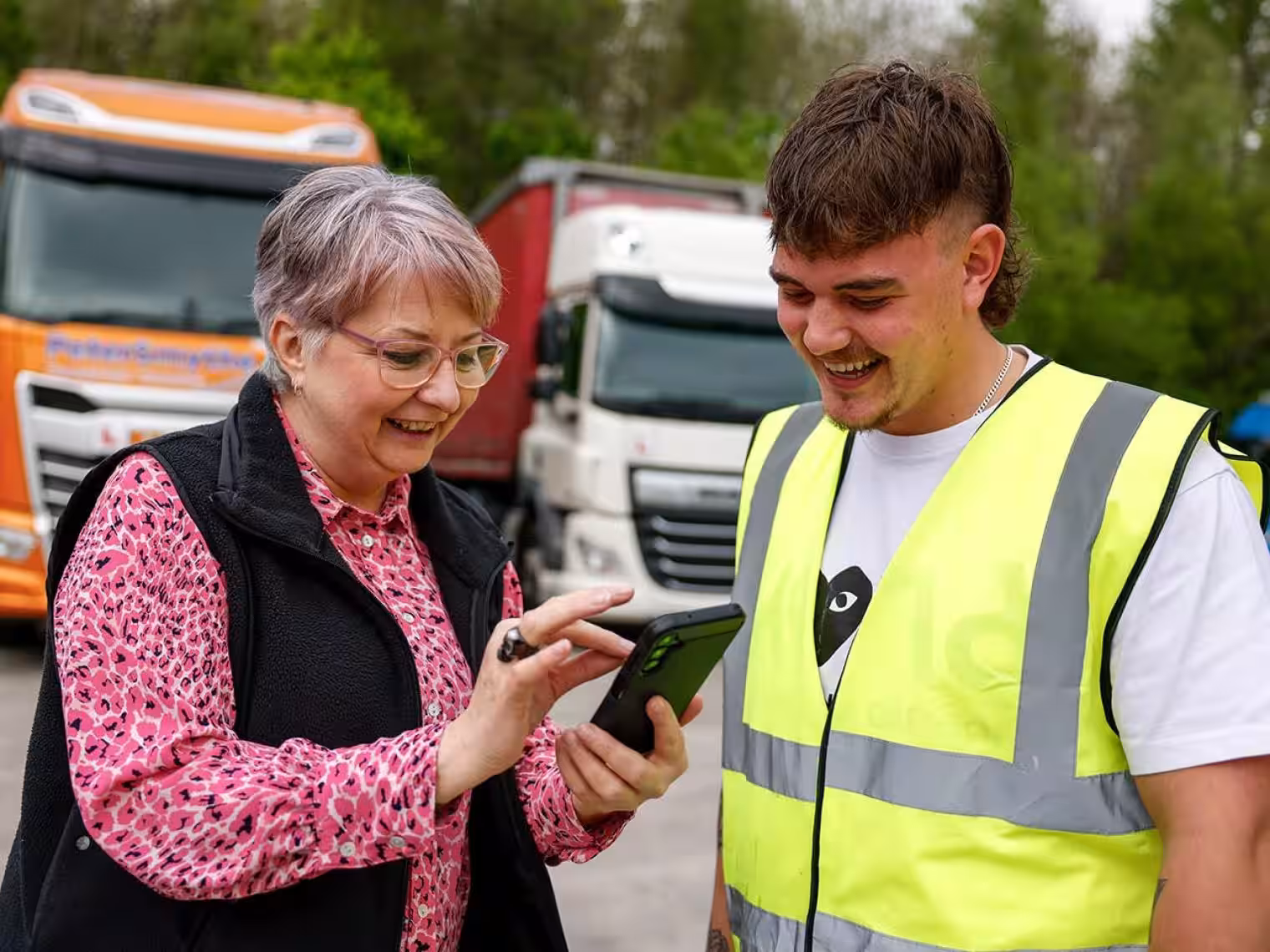 Image of two people looking at phone in front of HGV's used for transport training