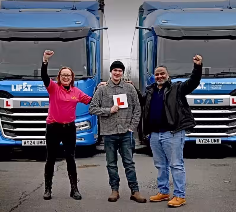 Image of Alex in front of two blue HGVs after passing HGV training course with Lifft