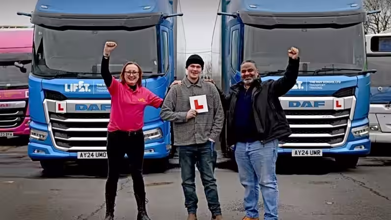 Image of Alex in front of two blue HGVs after passing HGV training course with Lifft